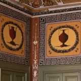 Le pareti laterali, delimitate da due porte verdi sovrastate da grandi riquadri con anfore scure...